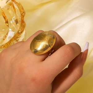 Anello ovale testurizzato in acciaio inossidabile dorato su mano con sfondo di seta