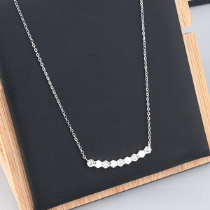 Detail view of hexagonal pendant necklace with zircon inlays on a black display stand