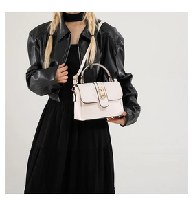 Minimalist beige crossbody bag with gold oval clasp on a model in a black leather outfit