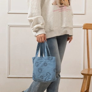 Détail d'un sac cabas en velours côtelé bleu avec un motif de visage souriant noir