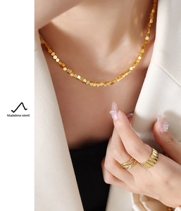 Close-up of golden stainless steel necklace with cube beads and wide ring on model