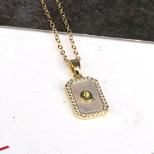 Close-up of square shell pendant necklace with 18K gold letter Q and cubic zirconia