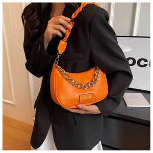 Detail of bright orange crescent bag with bold gold chain and woven shoulder strap