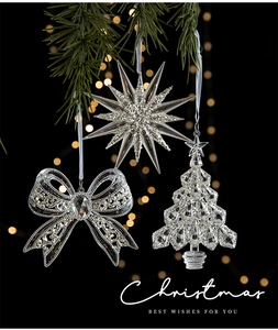 Close-up of clear acrylic Christmas star and tree ornaments with elegant golden bokeh light