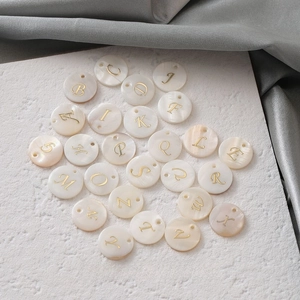 Detail of 26 round shell pendants with golden letters for DIY jewelry making