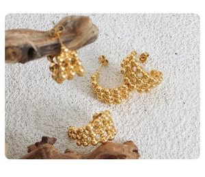 Detailed close-up of C-shaped gold beaded earrings on textured white background
