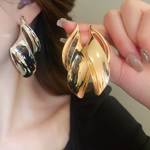 Detailed view of layered abstract wavy metal earrings in polished gold and silver finishes
