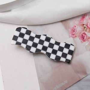 Close-up of a wave-shaped black and white checkerboard hair clip on floral background