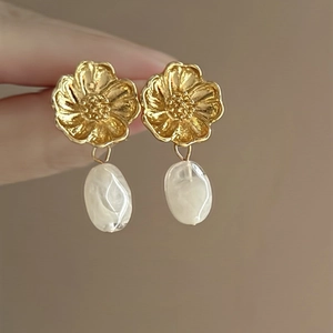 Detail of gold metal flower earrings with white pearl drop pendant and textured petals