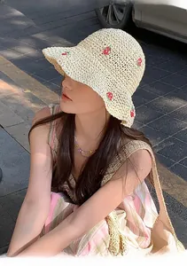 Detail of hand-woven beige straw hat with red strawberry embroidery and wavy brim