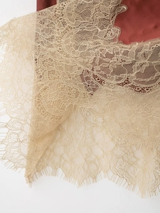 Detail of elegant champagne lace overlay on brick red satin fabric with eyelash fringe edge