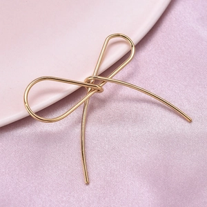 Macro view of a gold-plated stainless steel bow pendant on soft pink silk fabric