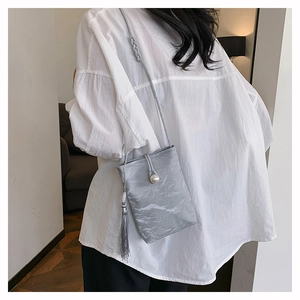 Petit sac bandoulière gris plissé avec perle et pompon porté par un mannequin femme