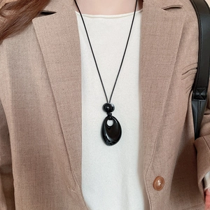 Close-up of black teardrop pendant necklace on model wearing a beige blazer suit