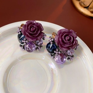 Detail view of purple rose stud earrings with crystals on a white ceramic plate