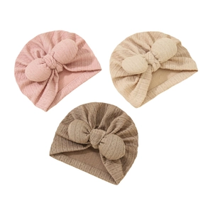 Detail of three baby knitted hats in pink, beige, and brown with bow ties and cable texture