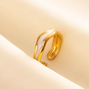 Dettaglio di un anello dorato ondulato con smalto bianco su sfondo di tessuto beige