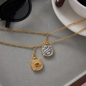 Close-up of a double-layered gold coin necklace on a grey velvet surface lifestyle setting