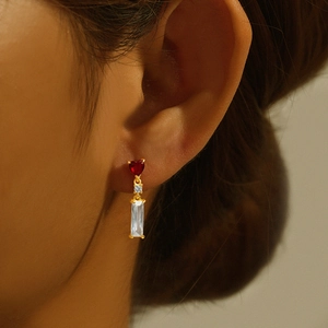Detailed close-up of gold earrings with red heart and rectangular crystals on a model