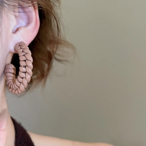 Close-up of model wearing a nude woven C-shaped earring with leather texture
