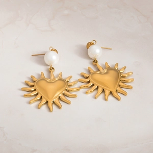 Detailed close-up of gold heart sun earrings with white pearls on marble texture