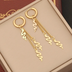 Macro view of gold snake pendant tassel earrings with layered chains on a jewelry box