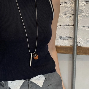 Detail of wooden acorn and silver bar pendant necklace on a model with white brick wall