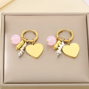 Detail of gold hoop earrings featuring pink beads and heart pendants on luxury base