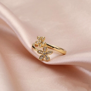 Detailed view of two gold floral rings with micro-set zircons on soft pink silk