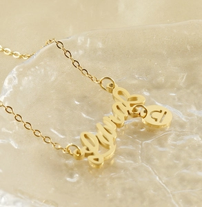 Macro shot of gold Libra zodiac pendant and custom script nameplate on wavy water surface