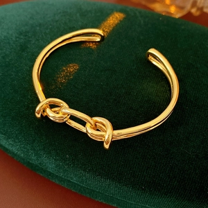Close-up of a gold-plated knotted open bangle on luxury dark green velvet surface