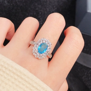 Cocktail ring with oval blue gemstone surrounded by crystals shown on a model's finger