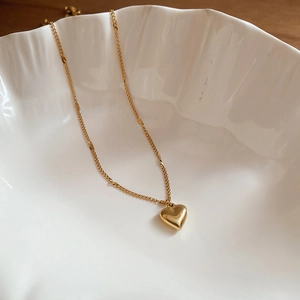 Close-up of golden zircon clover gourd pendant necklace on white artistic ceramic bowl