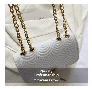 Détail d'un sac bandoulière blanc avec texture à vagues et bandoulière en chaîne dorée