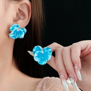 Dettaglio di orecchini a fiore con petali blu e centro con diamante sulla modella