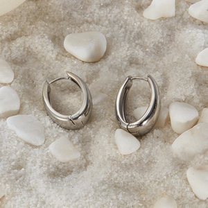 Detailed view of silver U-shaped hoop earrings on white sand with a polished finish