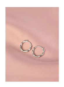 Macro shot of silver bamboo joint hoop earrings on elegant light pink satin fabric