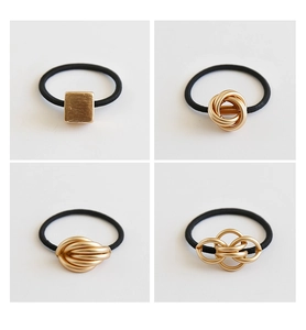 Detail of four golden metal hair ties with square and knot designs on black elastic bands