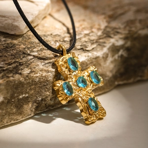 Gold 18k cross pendant necklace with blue crystals on a natural stone background