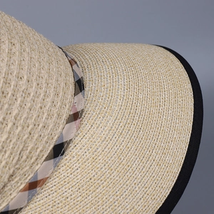 Close-up of beige woven straw hat featuring classic plaid ribbon and black piping detail