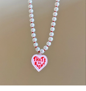 Detail view of pearl necklace with heart pendant featuring THAT'S ALL RIGHT inscription