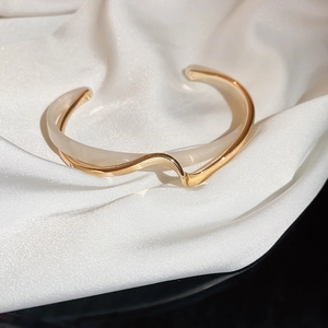Detail of wavy gold and ivory open bangle on white silk background with natural lighting