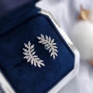 Macro shot of silver feather earrings with zircon inlays on blue velvet box