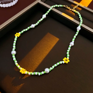 Close-up of green and white beaded necklace with yellow flower charms and gold clasp