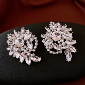 Elegant silver flower earrings with crystals on black display stand and brown silk