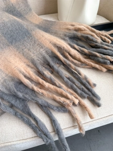 Detailed close-up of grey and brown plaid scarf tassels with soft cashmere-like texture