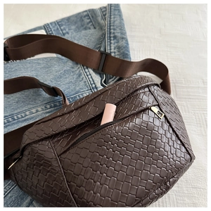 Detail of dark brown woven chest bag with golden zipper and lipstick for size reference