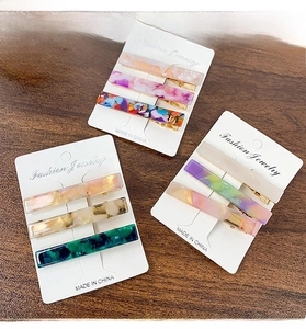 Detailed view of three elegant acetate hair clips with marble patterns on dark wood background