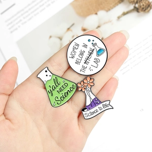 Close-up of three science enamel pins including Women Belong in the Lab slogan