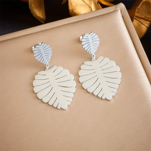 Macro detail of silver monstera leaf earrings on golden textured metallic surface